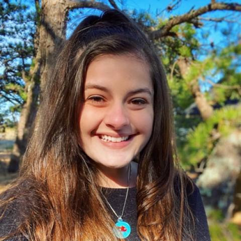 Dominique Mellone stands in front of a tree smiling at the camera