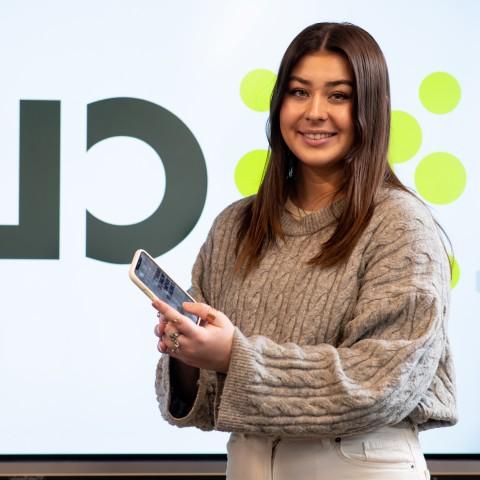 Abbie Anderson poses with a mobile phone. The name of her app, Clyk, is shown behind her